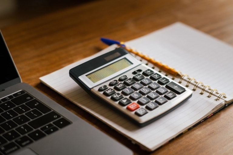 Calculadora sobre un cuaderno de anillas junto a un portátil, en una mesa de madera