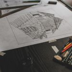Boceto a lápiz de un edificio sobre una mesa de dibujo, con escuadra, regla y lápices