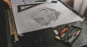 Boceto a lápiz de un edificio sobre una mesa de dibujo, con escuadra, regla y lápices