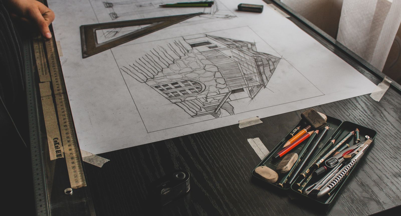 Boceto a lápiz de un edificio sobre una mesa de dibujo, con escuadra, regla y lápices
