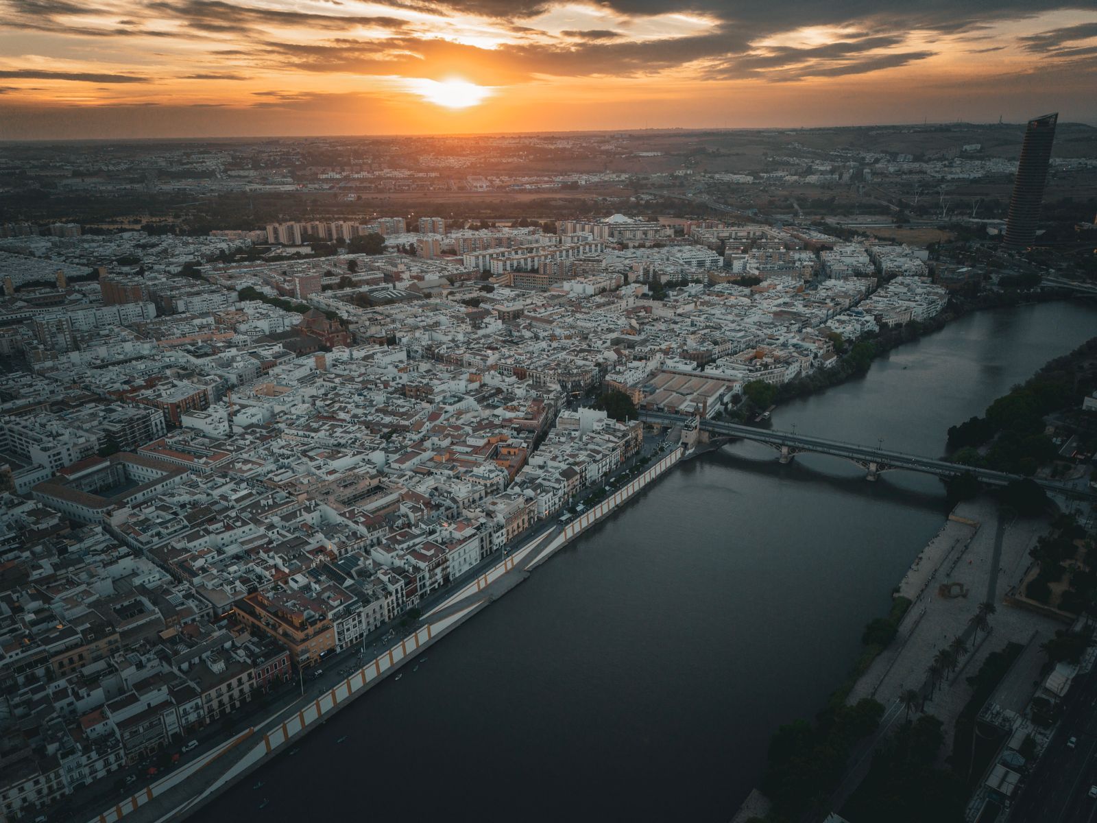 Vista aérea de Sevilla al atardecer, con el río Guadalquivir y los puentes en primer plano