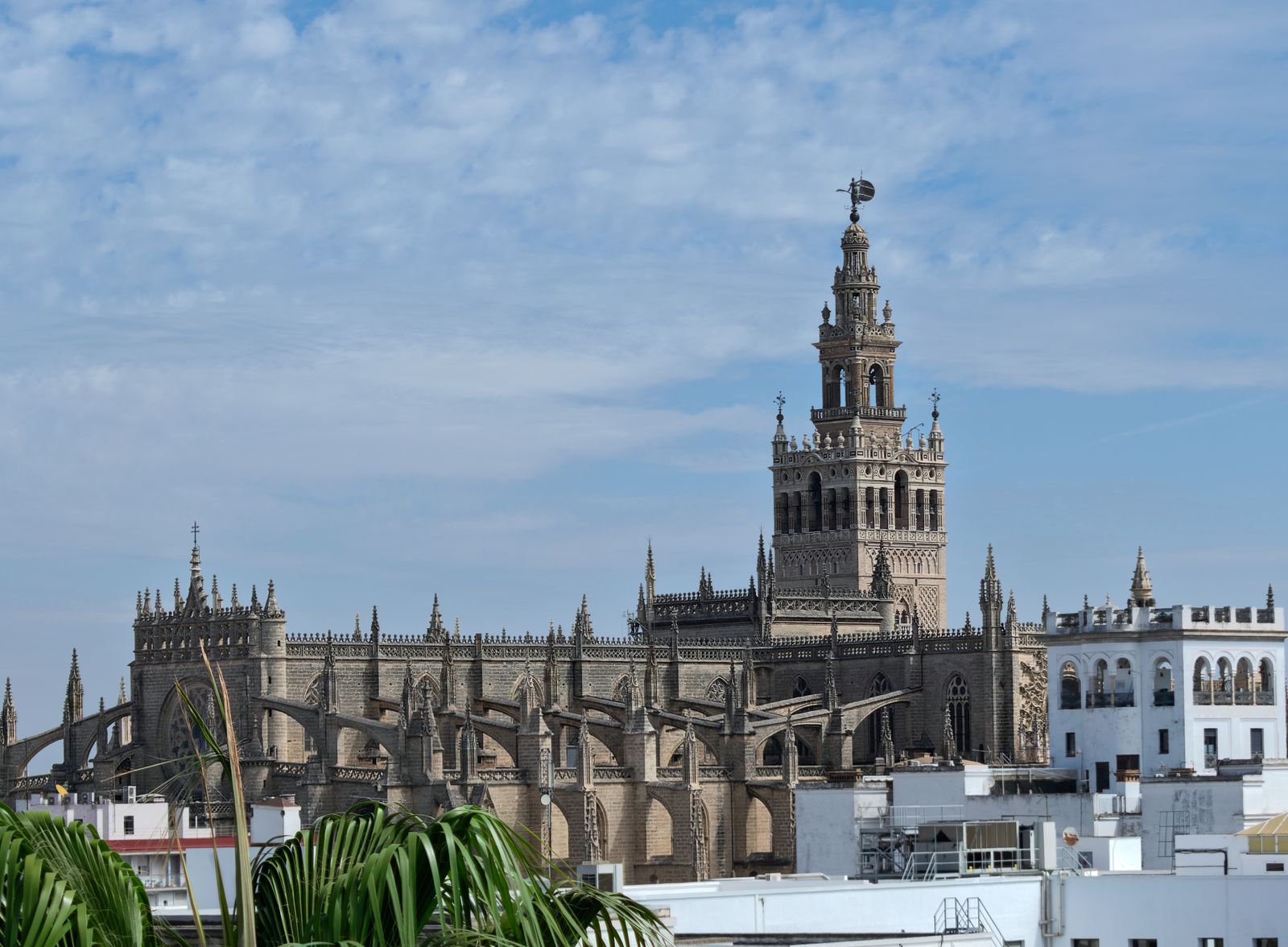 La Giralda y la Catedral de Sevilla vistas desde una azotea, con cielo azul y nubes