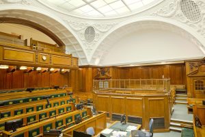 Interior de una sala de vistas sin público, con estrados y bancos de madera